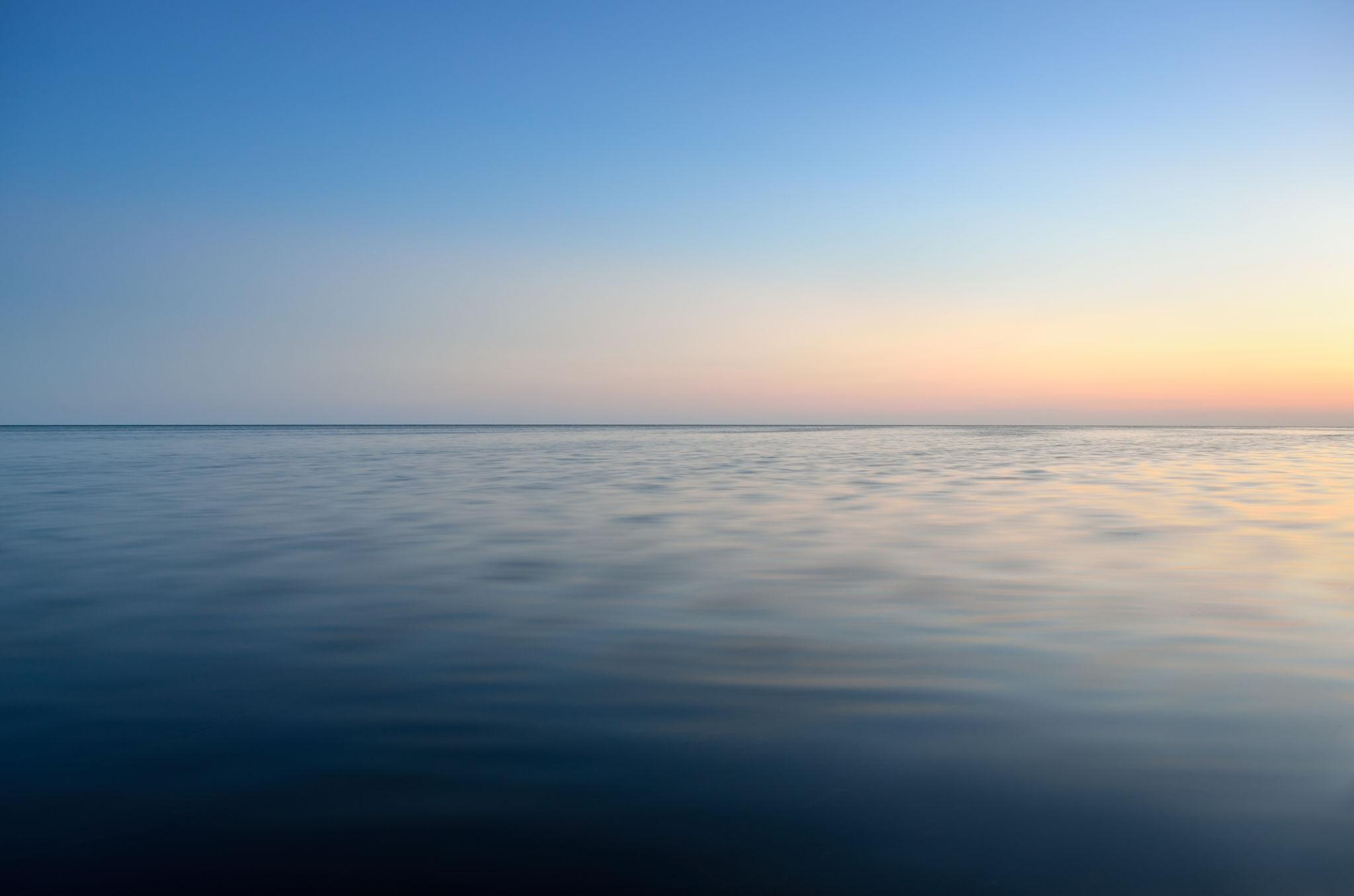 A still expanse of water at dusk, soft blue fading to warm peach at the horizon