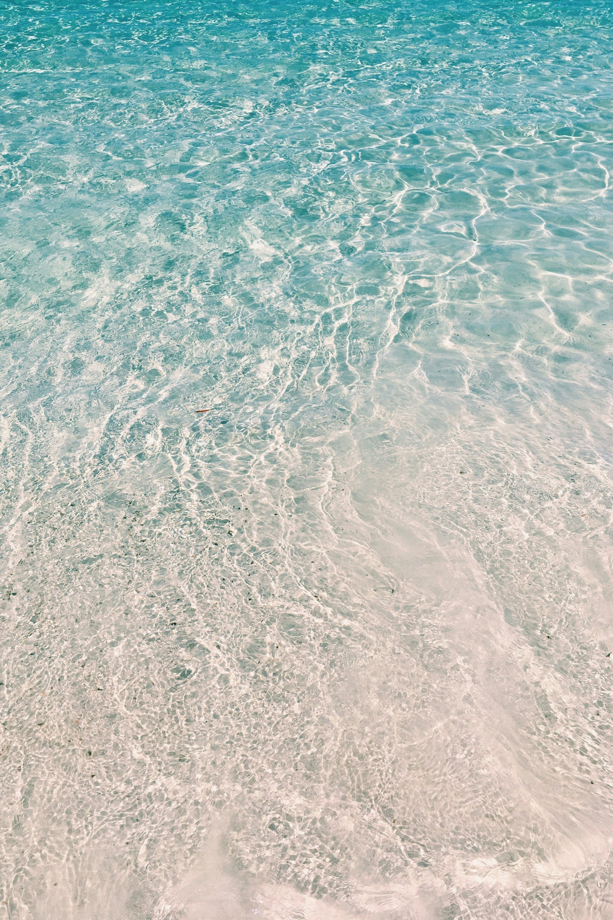 Clear shallow water over white sand, light refracting on the surface — evoking calm, hydration and clarity