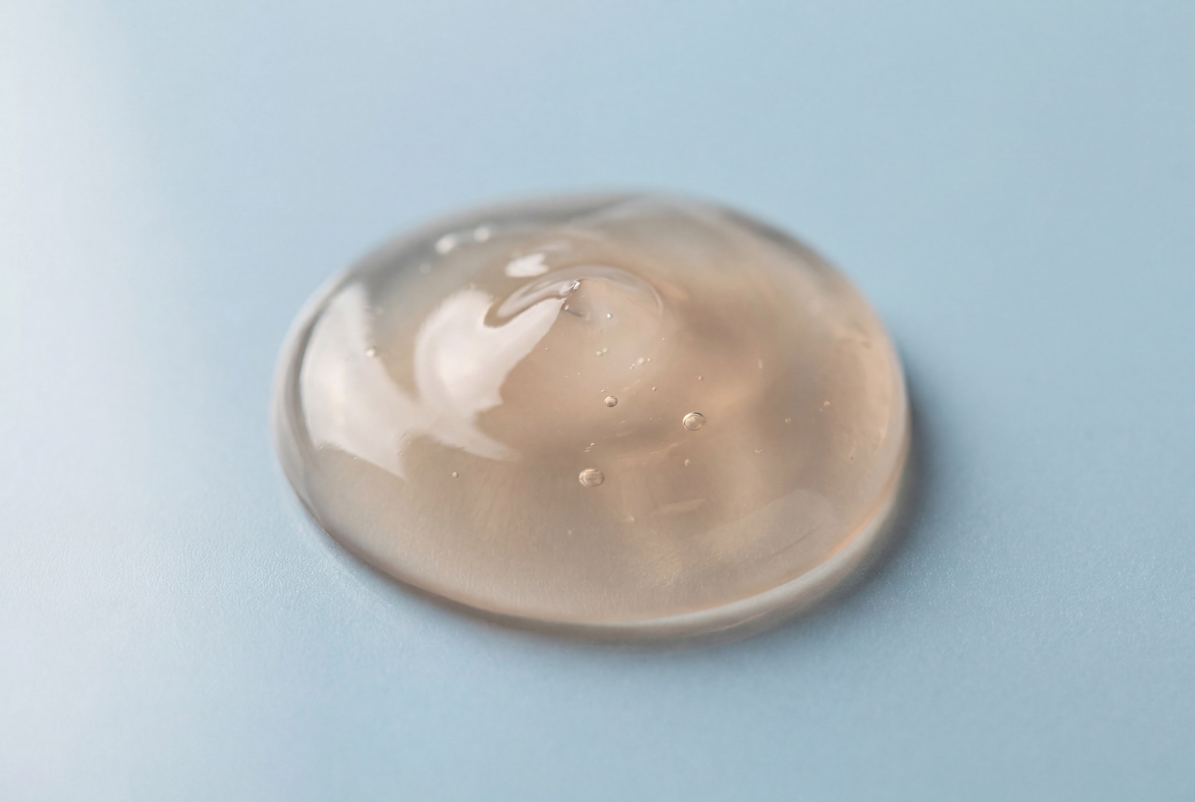 a single drop of clear gel on a pale blue surface